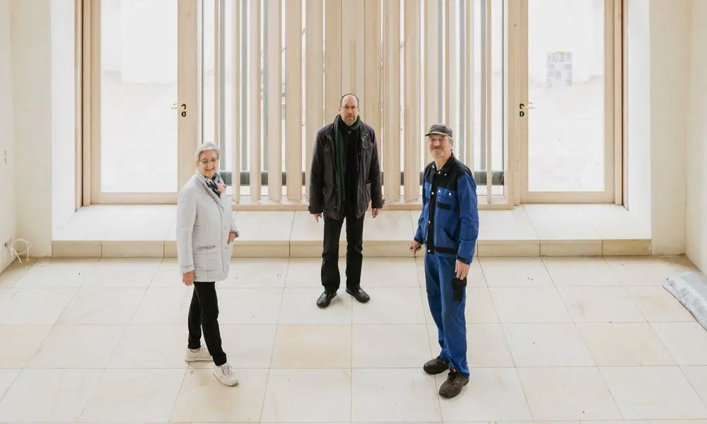 Hannelore Risse (links) und Ralf Zscherper (rechts) vom Förderverein mit Jochen Kinder (Mitte), Gemeindepastor bis 2018, vor der großen Glasfront im Innenraum der Kirche von Canitz